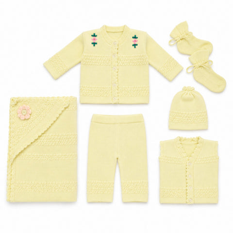 A coordinated baby knit clothing set laid out on a white background, including a cardigan, pants, hat, booties, and a blanket. The set is a pale buttery yellow with small embroidered floral details on the cardigan and a pink flower applique on the blanket.