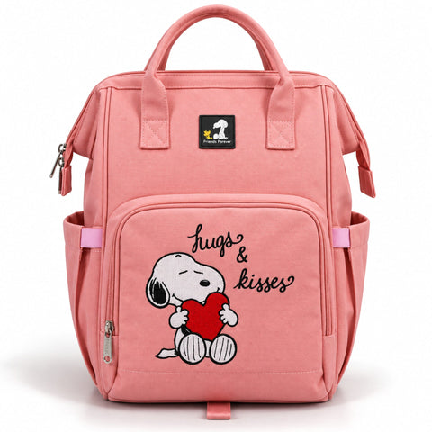 A pink canvas diaper bag featuring a front pocket with a cartoon Snoopy holding a red heart and the words 'hugs & kisses'. The bag has top handles, side pockets, and a black brand patch on the upper front.