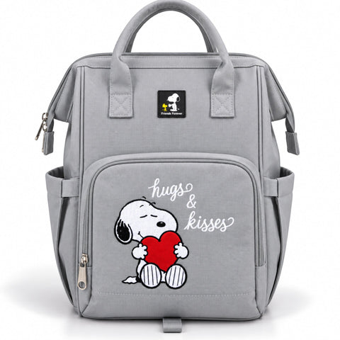 A light gray fabric diaper bag featuring a front pocket with a cartoon Snoopy holding a red heart and the words 'hugs & kisses' in white script. A black Snoopy logo patch is visible near the top handle, and the bag has dual top handles, side pockets, and zipper closures on a clean white background.