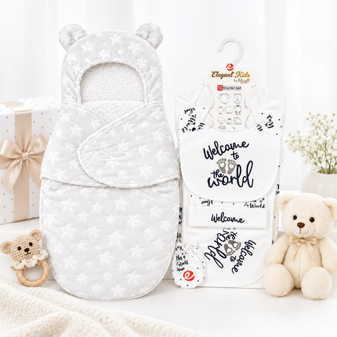 A baby gift set featuring a white quilted bassinet cover with star patterns and bear ears, shown next to its retail packaging. The packaging is labeled 'Elegant Kids Baby' and 'The Nursery Collection', and the set is styled with a cream teddy bear, a small wooden teething ring, and a gift box on a soft white background.