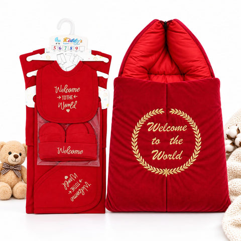 A red baby welcome gift set displayed both inside its retail packaging and unpackaged. The set includes a hooded quilted sleeping bag with gold embroidered text reading 'Welcome to the World' inside a laurel wreath, a matching bib, and a small pouch.