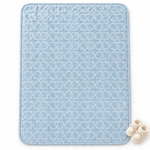 A light blue baby blanket or mat with a repeating white heart-quilted pattern, shown flat on a white background with a pair of cream baby booties in the bottom right corner.