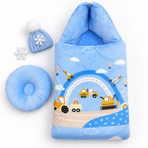 A baby footed sleeping bag set in light blue, featuring a playful winter-themed print with construction vehicles, clouds, and a blue knit pom-pom beanie, displayed on a clean white background alongside a matching circular pillow and snowflake accents.