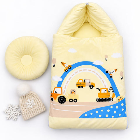 A baby winter sleeping bag set in pale yellow, featuring a colorful construction-themed print with a blue rainbow, yellow vehicles, and clouds. The set includes a matching pale yellow circular pillow, a beige knit beanie with a white pom-pom and snowflake, and a white snowflake ornament, all arranged on a clean white background.