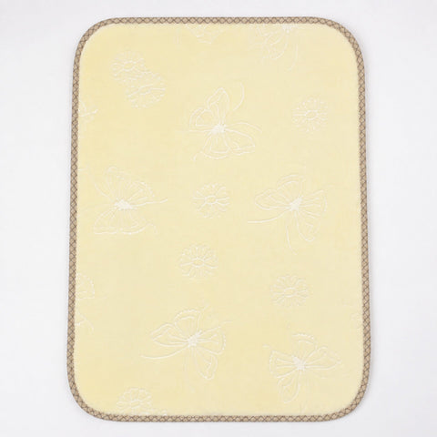 A pale yellow rectangular mat with rounded corners, featuring a subtle white embroidered butterfly and floral pattern and a braided tan border, shown on a plain white background.