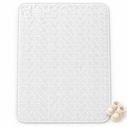 A white rectangular baby blanket or changing pad with a quilted circular pattern, shown flat on a white background with a pair of cream knit booties in the bottom right corner.
